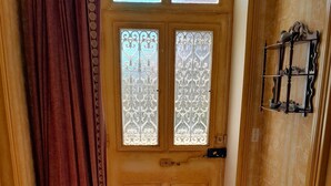 Une pièce dotée d’un sol carrelé à motifs, d’une porte en bois ornée de panneaux de verre décoratifs et d’un rideau.