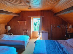 A cozy attic bedroom with wooden walls and sloped ceilings. There are two beds with blue bedding, a small table with a lamp, and a window with curtains. - Creuse, Large character house in quiet area with terrace, swim. pool and garden (Auzances)