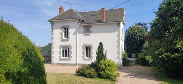 A two-story white building with a sloped roof, a chimney, and a small garden area with a pathway leading to the entrance. - Creuse, Large character house in quiet area with terrace, swim. pool and garden (Auzances)