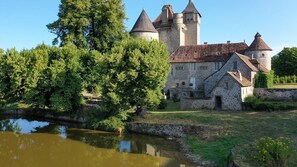 A historic stone building with a moat, surrounded by lush greenery and a clear sky. - Creuse, Large character house in quiet area with terrace, swim. pool and garden (Auzances)