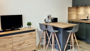 A modern kitchen with a wooden countertop, two bar stools, a coffee machine, and a television on a wooden cabinet. - Renovated Studio 4 pers. at ski slopes with parking (La Joue du Loup)