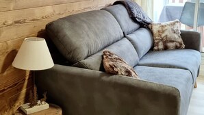 A grey sofa with two decorative pillows, a lamp, and a small wooden sculpture on a side table. - Renovated Studio 4 pers. at ski slopes with parking (La Joue du Loup)