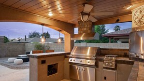 Eine Außenküche mit Gasgrill, Backofen und einer Arbeitsplatte aus Stein.