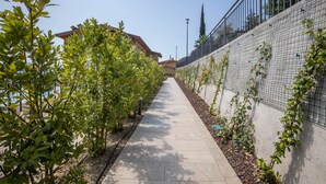 Un sendero bordeado de vegetación, una valla metálica y un edificio al fondo.