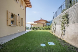 Un patio con césped, un edificio con balcón y una valla.