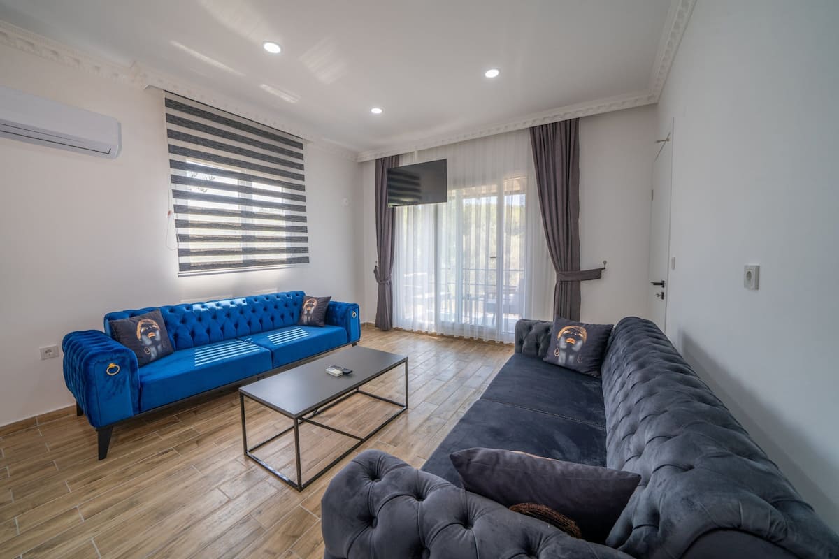 Uma sala de estar com um sofá azul, um sofá cinza e uma mesa de centro.