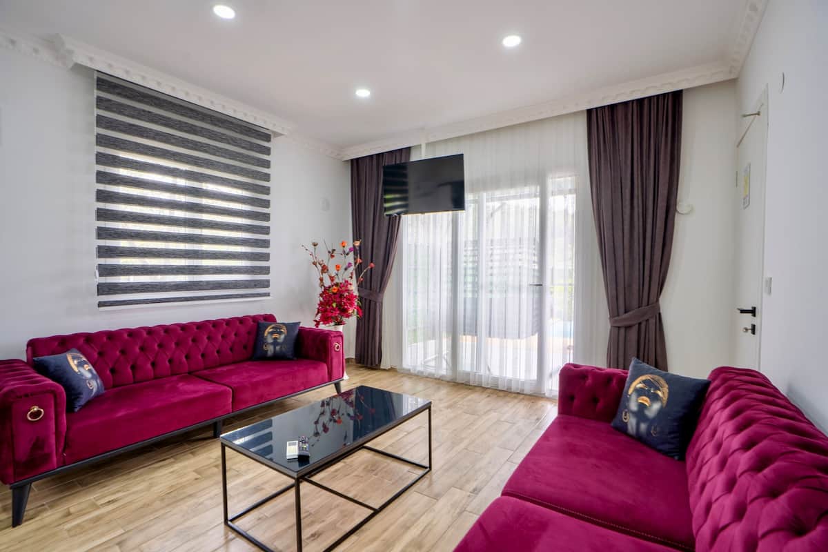 Uma sala de estar moderna com um sofá vermelho, uma mesa de centro de vidro e uma janela grande com cortinas.