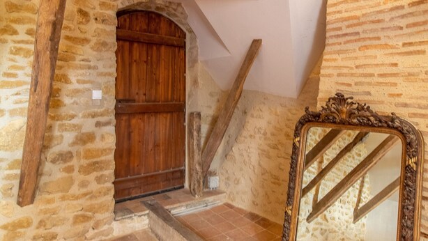 A rustic stone interior with a wooden door, a mirror, and a staircase.