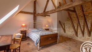A bedroom with a sloped ceiling, a wooden bed frame, a bedside table with a lamp, a chair, and a small table.