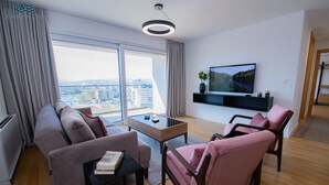 A modern living room with a sofa, two pink chairs, a coffee table, and a TV on the wall. - River Walk Sarajevo (Sarajevo)