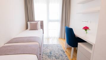 Un dormitorio con cama, escritorio y silla. Hay una ventana con cortinas y un jarrón con flores sobre el escritorio.