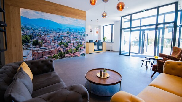 A spacious lobby with a large cityscape mural, comfortable seating, and a reception desk. - River Walk Sarajevo (Sarajevo)