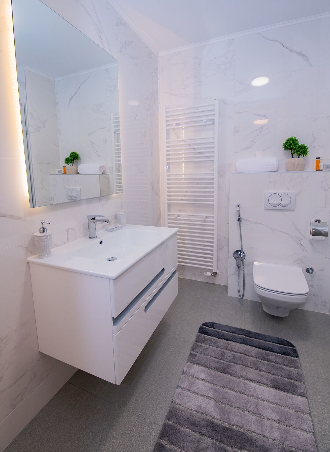 A modern bathroom with a white vanity, a toilet, a shower, and a large mirror.