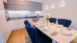 A modern kitchen with white cabinets, a black countertop, and a dining area with a white table set for four. - River Walk Sarajevo (Sarajevo)