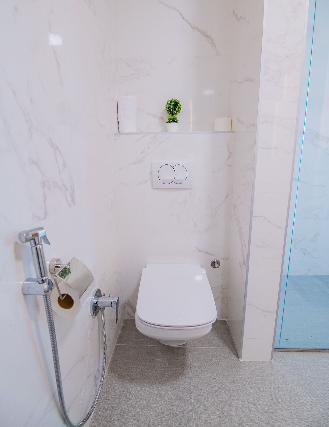 A compact bathroom with a toilet, a shower, and a small shelf with toiletries.