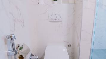 A compact bathroom with a toilet, a shower, and a small shelf with toiletries.