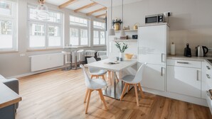 A modern kitchen with a dining area, wooden flooring, white cabinetry, and a built-in microwave. - The sea always works - Winterstrasse 23 (Norderney)