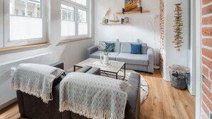 A modern living room with a grey sofa, two armchairs, a coffee table, and a large window with blinds. - The sea always works - Winterstrasse 23 (Norderney)