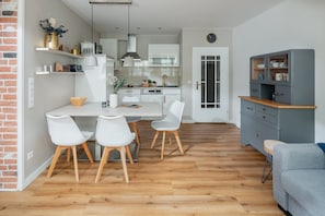 Eine moderne Küche mit weißen Schränken, einem Holztisch mit vier Stühlen und einem grauen Schrank mit Glastüren.