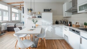 A modern kitchen with white cabinets, a dining table with chairs, and a coffee maker. - The sea always works - Winterstrasse 23 (Norderney)