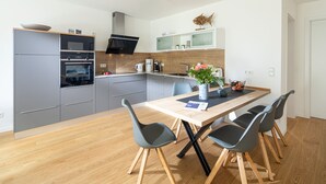 A modern kitchen with grey cabinets, a built-in oven, and a microwave. There is a dining table with four chairs and a vase with flowers. - // VACATION APARTMENT CLOUDLESS // (Norderney)