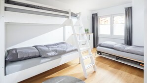 A modern, well-lit room with bunk beds, a ladder, a small table with a plant, and a window with curtains. - // VACATION APARTMENT CLOUDLESS // (Norderney)