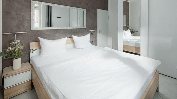A modern bedroom with a large bed, bedside tables, a mirror, and a potted plant. - // REGINA MARIS - APARTMENT 1 // (Norderney)