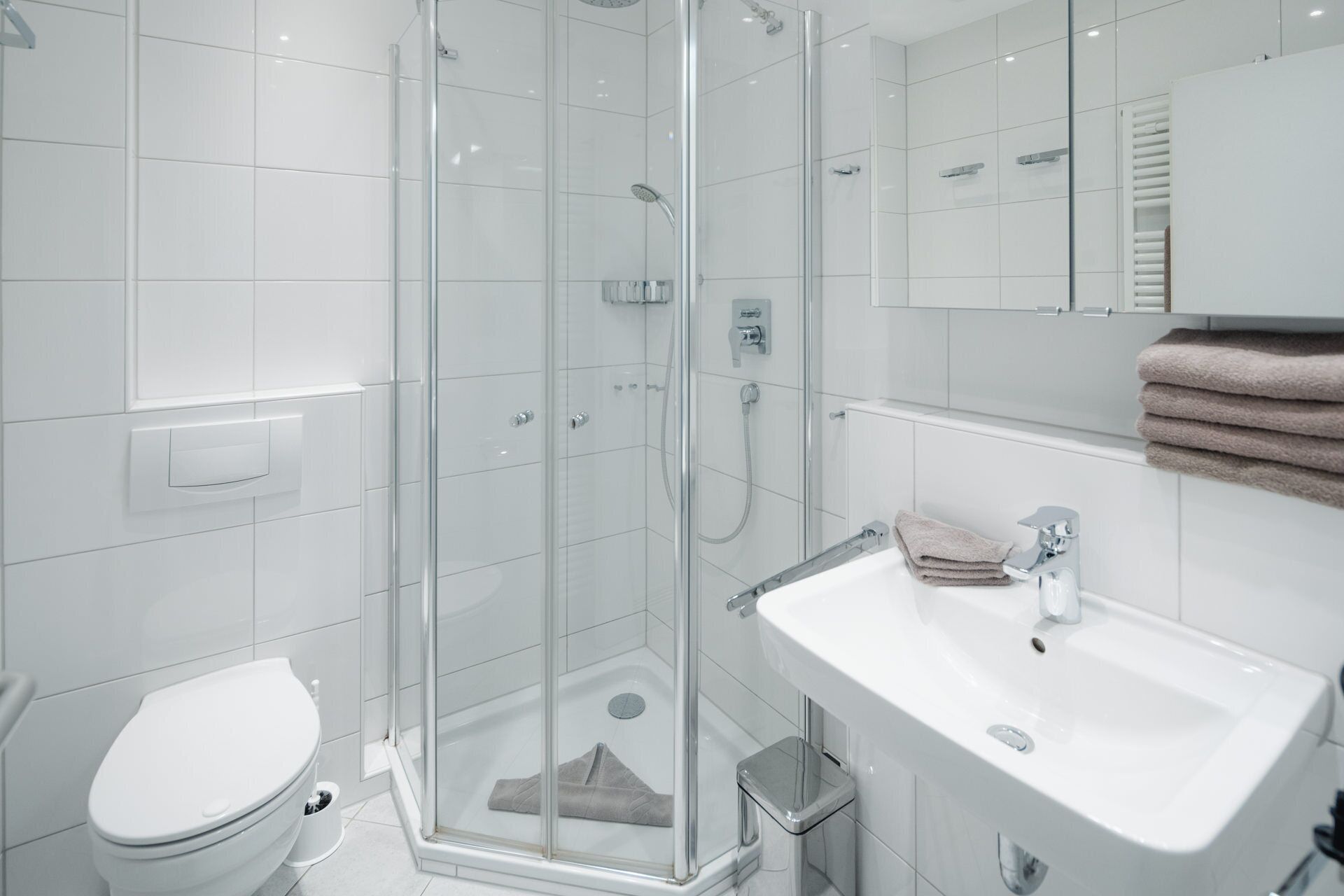 Ein modernes Badezimmer mit einer Duschkabine, einem weißen Waschbecken und einer Toilette.