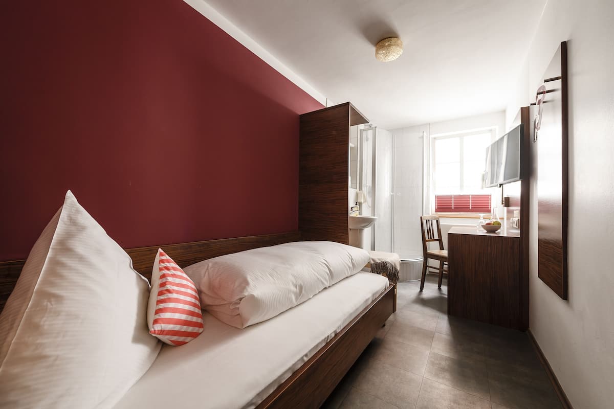 A bedroom with a bed, a wooden headboard, a red wall, a desk, a chair, and a television.