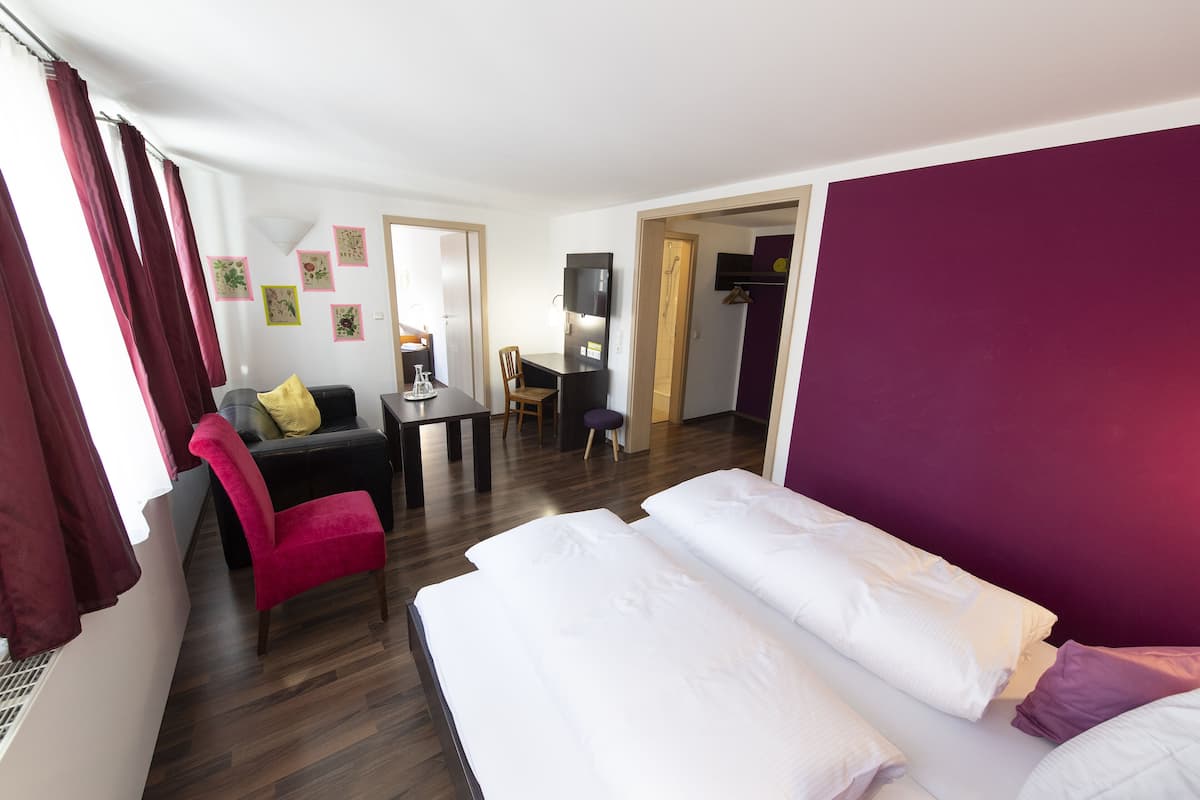 A hotel room with a bed, a desk, a chair, and a sofa.