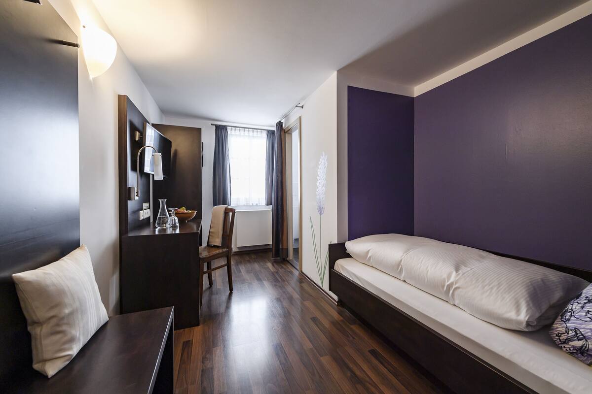 A modern hotel room with a bed, a desk, a chair, and a window with curtains.