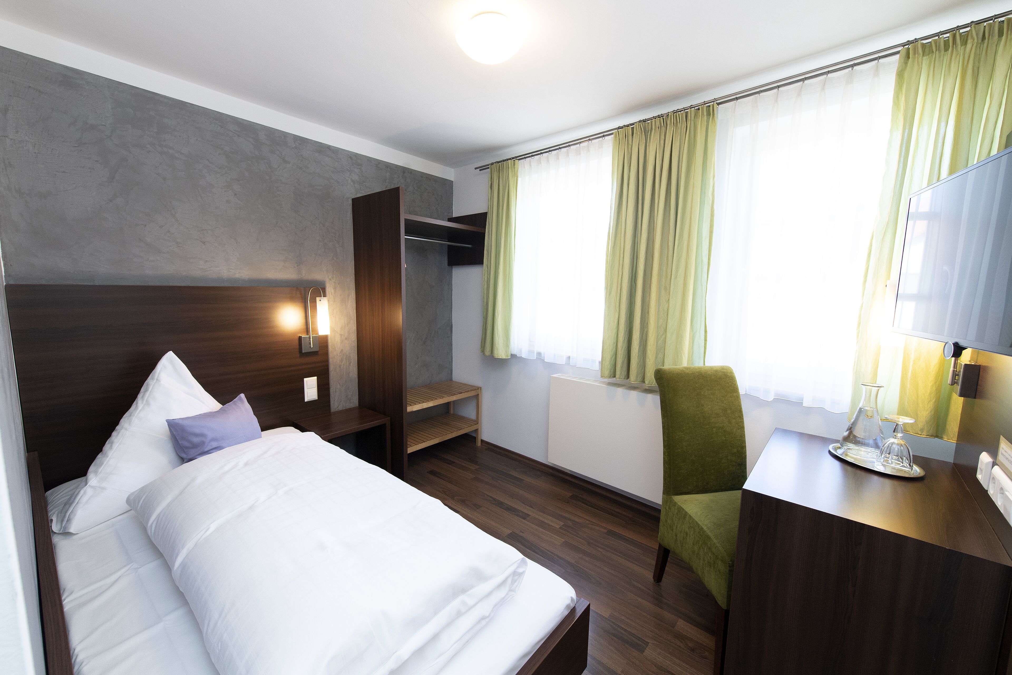 A hotel room with a bed, a desk, a chair, a wardrobe, and a window with curtains.