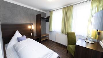 A hotel room with a bed, a desk, a chair, a wardrobe, and a window with curtains.
