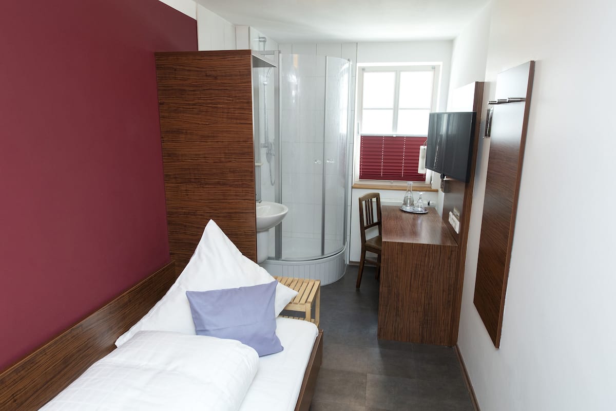A hotel room with a bed, a wooden desk, a shower, and a TV.