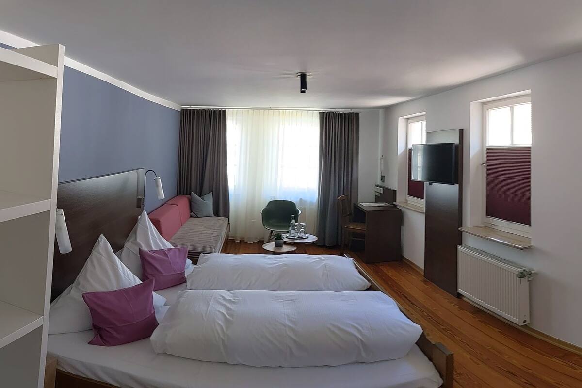 A hotel room with two beds, a desk, a chair, a TV, and a window with blinds.