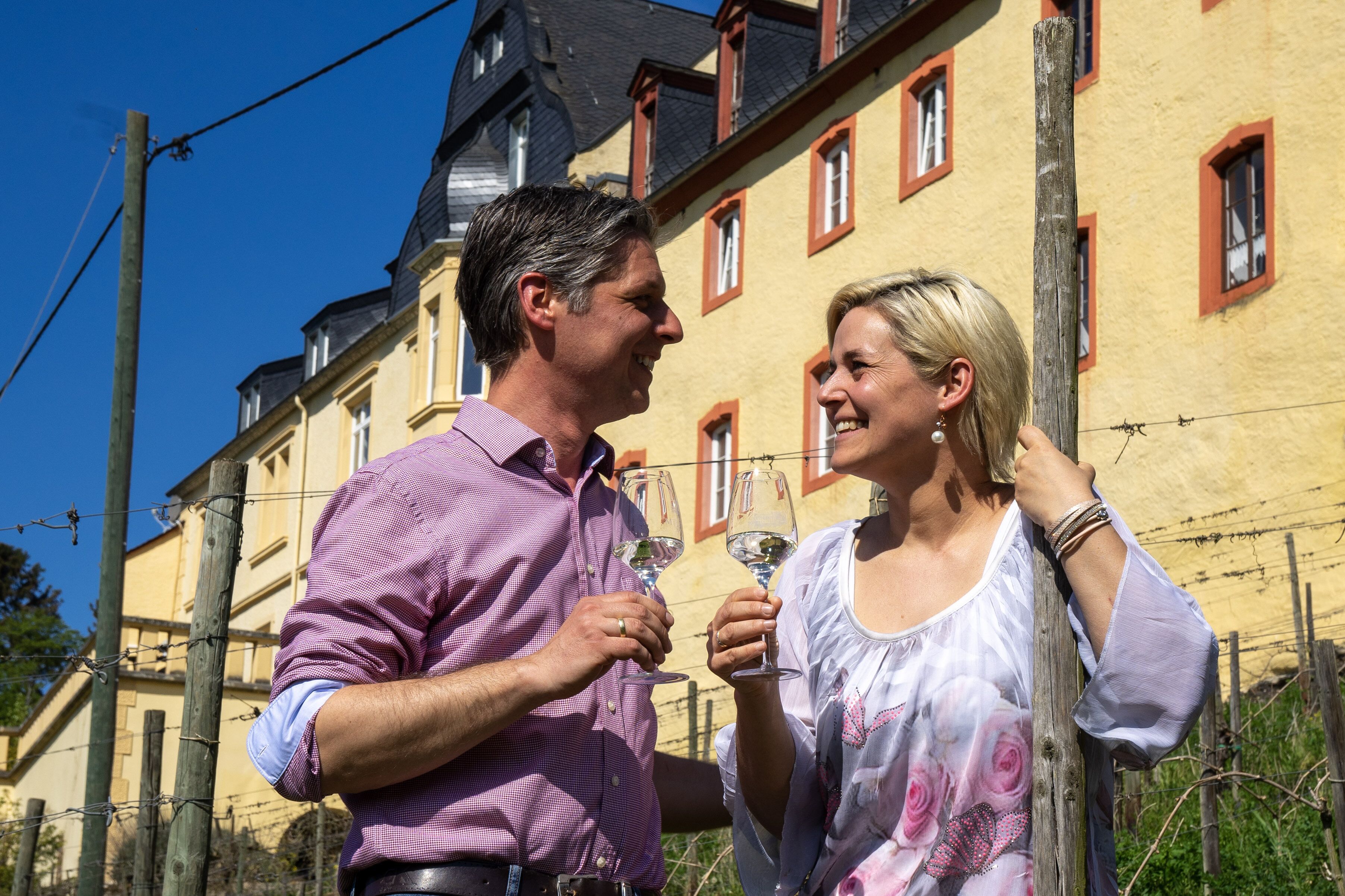 Un homme et une femme se tiennent devant un bâtiment à la façade jaune et aux encadrements de fenêtres rouges.