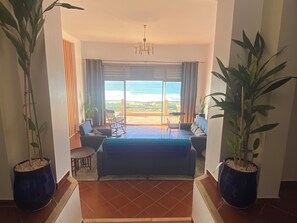 A room with a large bed, two chairs, a table, and a view of the ocean.