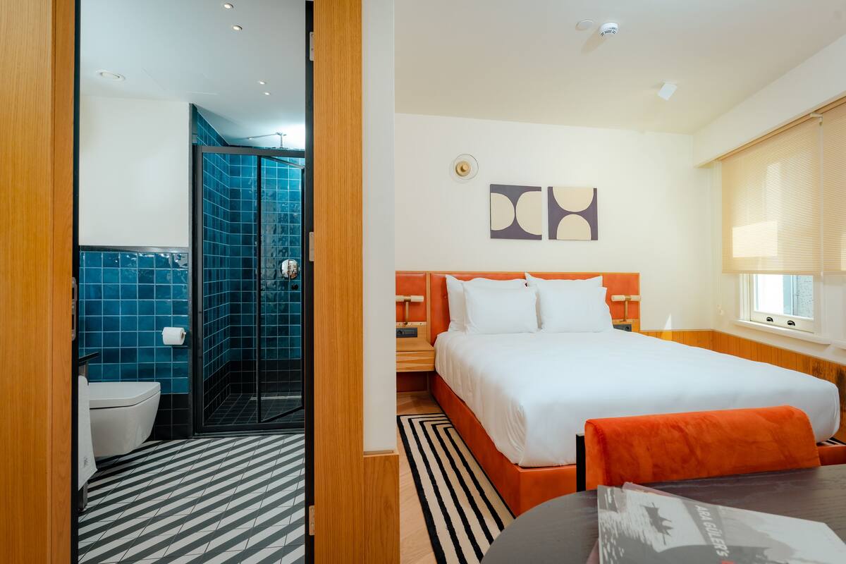 A hotel room with a bed, a bathroom with a shower, and a dining area.