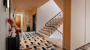 A modern hotel lobby with a geometric patterned floor, a staircase with black railings, and a reception desk with a vase of red flowers. - The Gift Hotel (Istanbul)