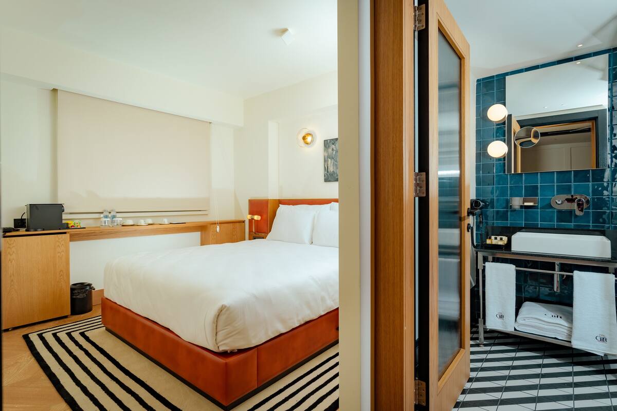 A hotel room with a bed, bedside table, and a bathroom with a sink and mirror.