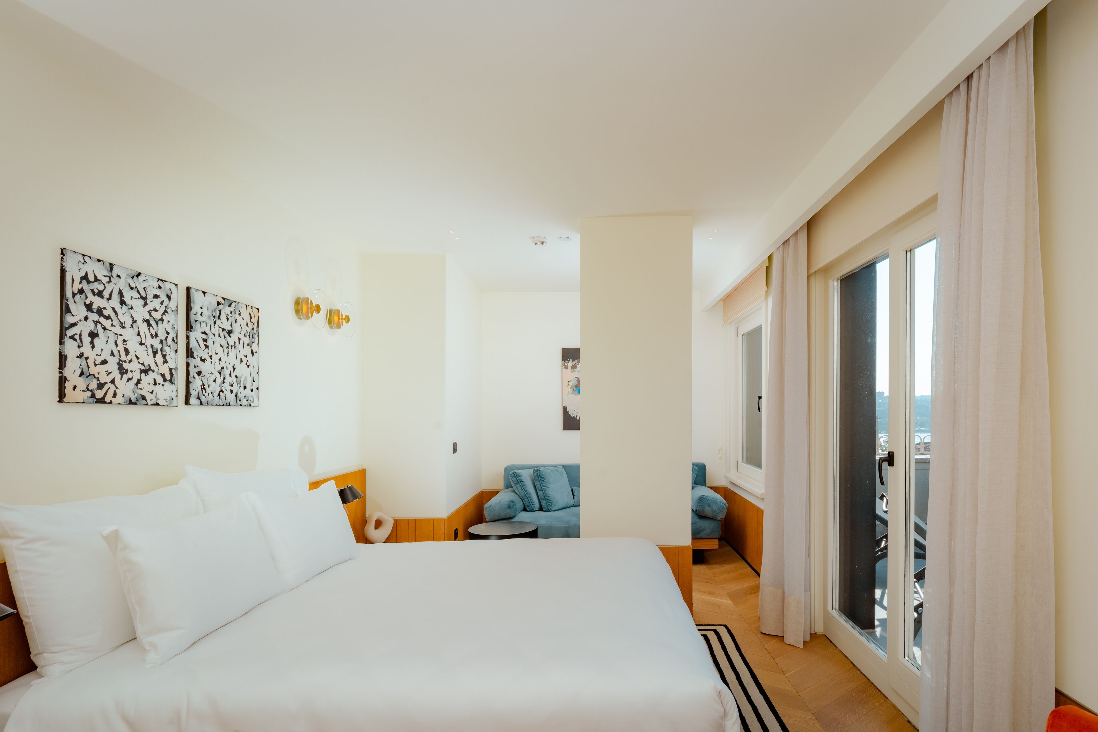 Habitación de hotel con una cama grande, una zona de estar pequeña con un sofá azul y un balcón con vistas.