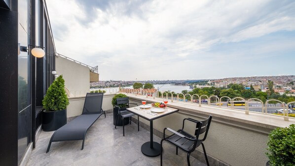 A balcony with a table and chairs, overlooking a cityscape and river.
