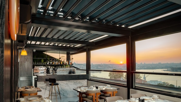 A restaurant with tables set for dining, a bar area, and a view of the sunset over a body of water. - The Gift Hotel (Istanbul)