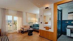 A modern hotel room with a large balcony, a sofa, a coffee table, and a bathroom with a blue tiled wall. - The Gift Hotel (Istanbul)