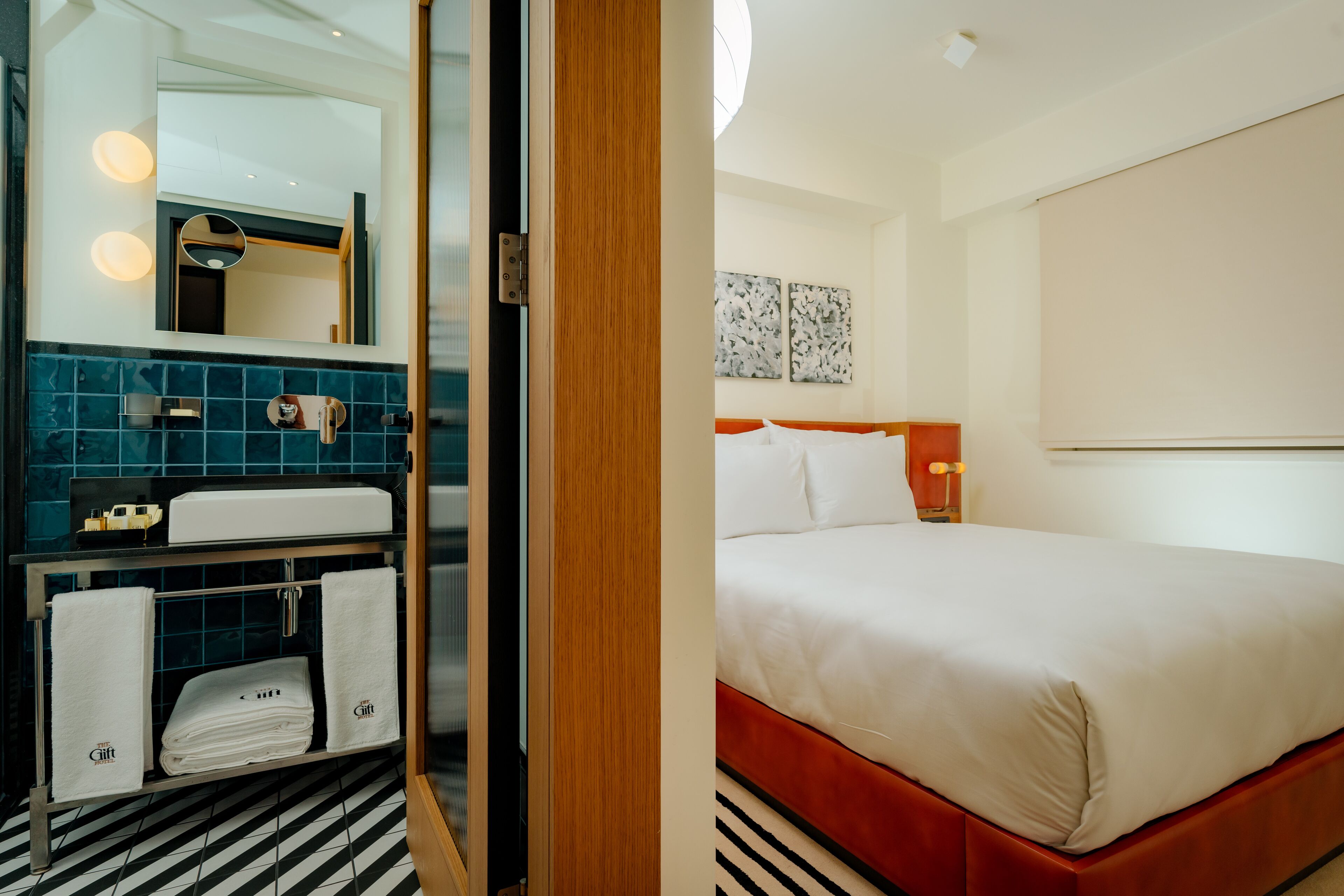 A hotel room with a bed, a bathroom with a mirror, and a shelf with towels.