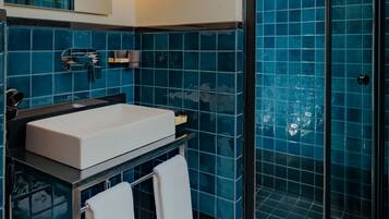 Un baño moderno con un lavamanos blanco, azulejos azules, cabina de ducha de vidrio y piso a cuadros blanco y negro.