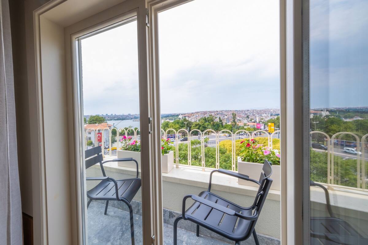 A balcony with two chairs, a view of a cityscape, and a clear sky.