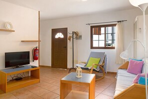 A living room with a television on a wooden stand, a rocking chair, a sofa, and a small table.