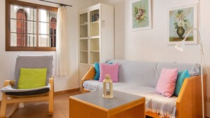 A living room with a wooden rocking chair, a grey sofa with colorful cushions, a white cabinet, and a small table with a lantern. - Holiday Home 'Cottage Santa Lucía 1' with Terrace, Shared Garden & Wi-Fi (Santa Lucía de Tirajana)