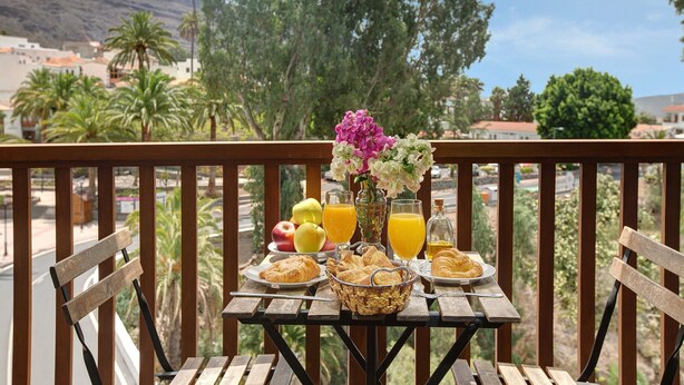 A wooden table with breakfast items, a vase of flowers, and a view of a mountainous landscape. - Holiday Home 'Cottage Santa Lucía 1' with Terrace, Shared Garden & Wi-Fi (Santa Lucía de Tirajana)